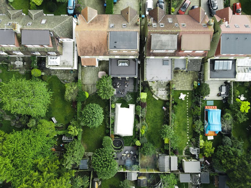 An aerial view of a residential neighborhood showing multiple back gardens separated by fences, each with distinct landscaping features. The gardens include well-maintained lawns with trimmed grass, p